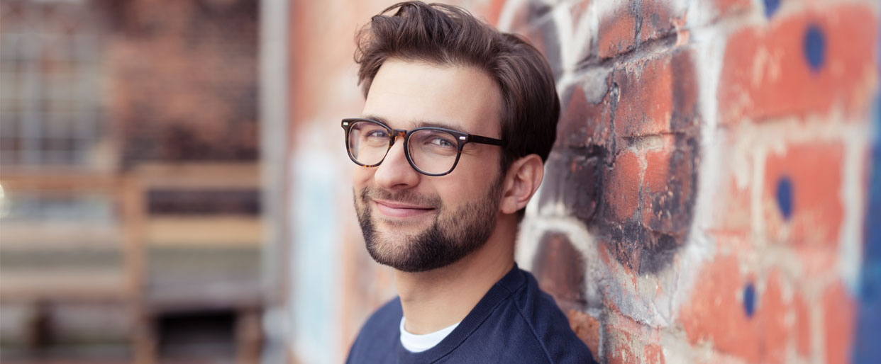 man leaning against wall wearing glasses